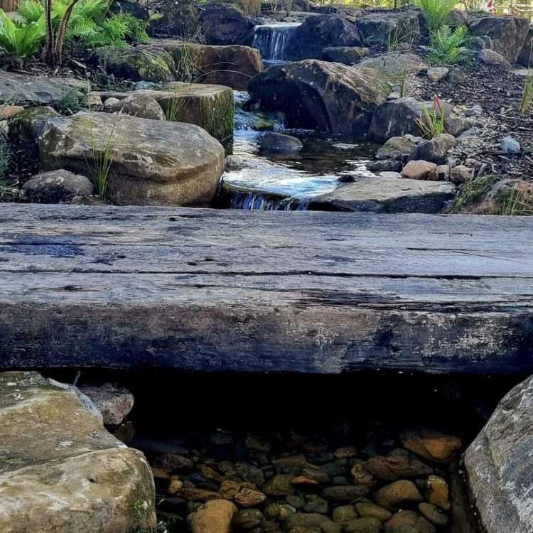 Railway sleeper being used as a bridge laying across a small garden stream.
