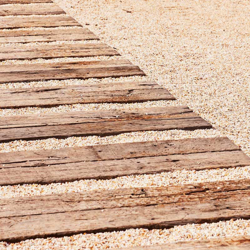 Pathway featuring railway sleepers and small stones. Sustainable luxury design.
